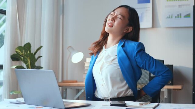 Office worker suffering back and neck pain from prolonged desk work, showing discomfort and stretching in an attempt to alleviate the pain