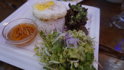 Vietnamese cuisine consisting of rice, fried eggs, vegetable pieces mixed with shallots, a bowl of Vietnamese chili sauce and grilled beef ribs at a Vietnamese restaurant
