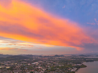 An aerial view of the Phuket islands bathed in soft pastel hues during sunset. The tranquil sea below is dotted with islands, while the sky above is painted with delicate pink and orange clouds.