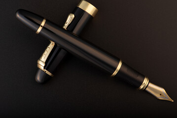 Fountain pen, beautiful black and gold fountain pen, positioned on dark background, selective focus.