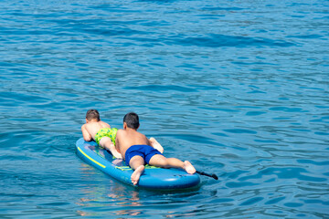 Two happy Teenage children, siblings paddle blue paddleboard together, enjoying active summer holidays, vacation Water adventure, parental supervision, water safety