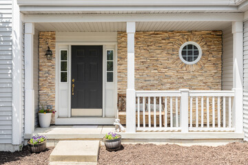 A front door detail with a stone accent wall, a black door, covered porch, white posts and railing,...
