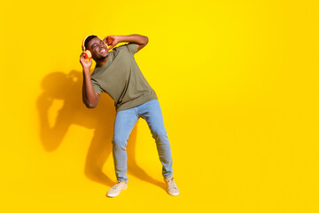 Photo of cheerful positive funky man wear khaki clothes listen music dance empty space isolated on yellow color background