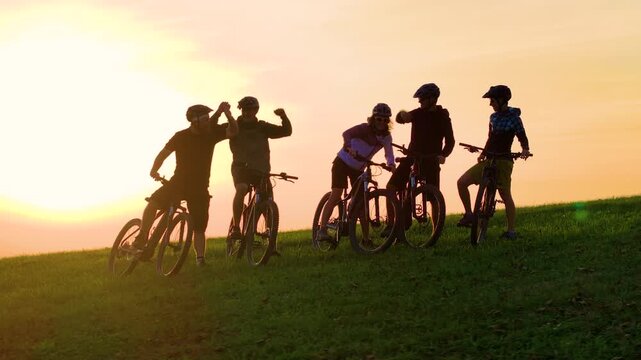 AERIAL, LENS FLARE: Group of sporty friends mountain biking in the sunny hills of Slovenia celebrate their awesome ride. Cheerful bike riders high five after a picturesque evening ride in the Alps.