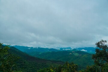 The sky is cloudy and the mountains are covered in green trees