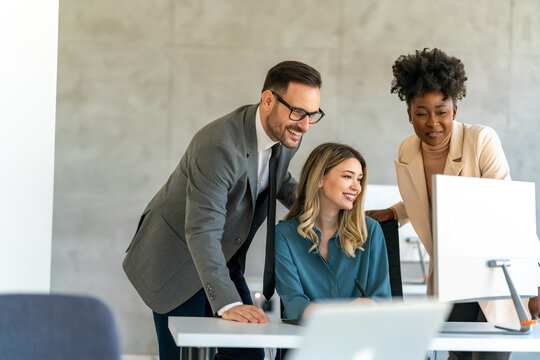 Group of happy multiethnic business people in formal wear gathered around computer in office