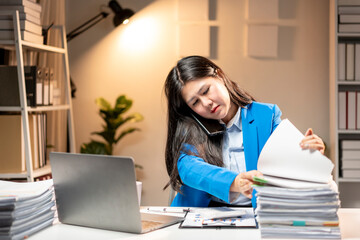 A woman in a blue jacket is on the phone in a cluttered office