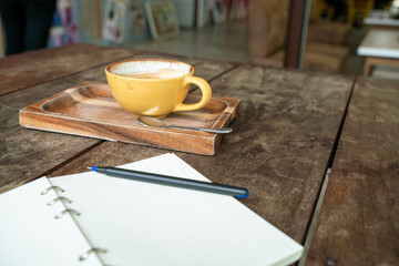 Hot latte coffee cup on wood table with blank notebook