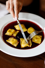 delicious dish of ravioli with juicy meat, served on a beautiful white plate next to a glass of red wine on a wooden table in a cozy, charming restaurant