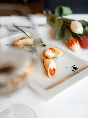 delicious pancake with juicy salmon, cream cheese, and fragrant herbs, served on a beautiful white plate next to colorful roses and a glass of white wine in a cozy, charming restaurant
