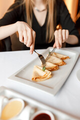 handsome girll is eating delicious dish of pancakes with various sauces, accompanied by a fragrant cup of coffee in a white mug, on a wooden table in a cozy, charming restaurant