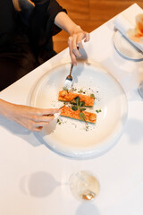 cute girl is eating a delicious dish with juicy salmon, fresh vegetables, avocado, and fragrant herbs, served on a beautiful white plate on a wooden table in a cozy, charming restaurant