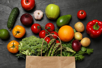 Vegan food delivery. Paper bag with different fresh vegetables and fruits on dark textured table, flat lay