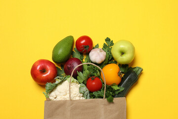 Delivery of vegetarian products. Paper bag with different vegetables and fruits on yellow background, top view