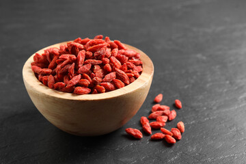 Dried goji berries in bowl on dark textured table, closeup