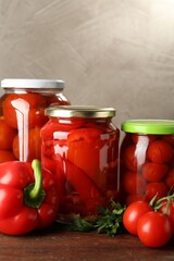 Different pickled vegetables in jars and fresh ingredients on wooden table