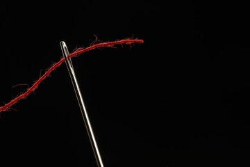 Sewing needle with red thread on black background, closeup. Space for text