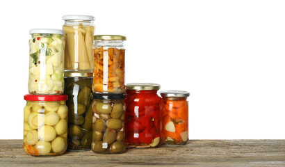 Different pickled products in jars on wooden table against white background. Space for text