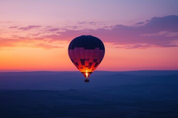 Fototapeta premium Hot air balloon silhouette captured at the peak of sunrise. The sky is a soft gradient of purples, blues, and oranges, creating a perfect backdrop for the balloon. The wide-open space around the