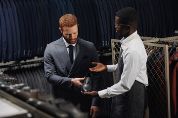 Salesman help for client in mens store. Young handsome man businessman in suit shopping classic shoes