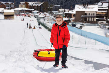 In winter, a happy boy rides snow tubing, inflatable slide in the mountains. Lifts the tubing up.