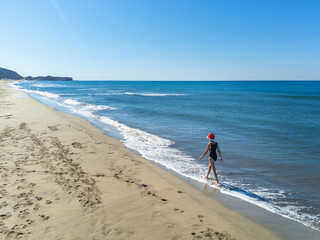 Young beautiful slender woman in Santa Claus hat running on sandy beach, dancing around herself, rejoicing in Christmas or New Year. Shooting with drone. Weekend Sea or Ocean. Resort Vacation.