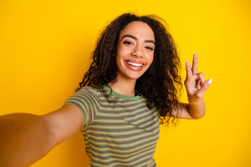Photo of toothy beaming girl with wavy hairstyle dressed striped t-shirt making selfie show v-sign...
