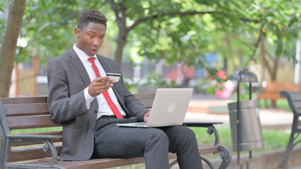 African Man Upset by Online Banking Failure with Laptop in Lap Outdoor