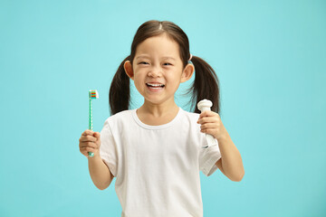 Beautiful asian ethnicity kid girl holding toothbrush and toothpaste tube, wearing in white t...
