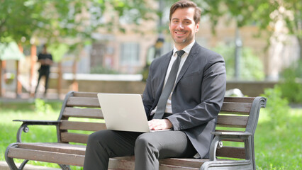 Middle Aged Businessman Smiling at Camera while Using Laptop Outdoor