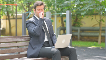 Businessman Coughing while Using Laptop Outdoor