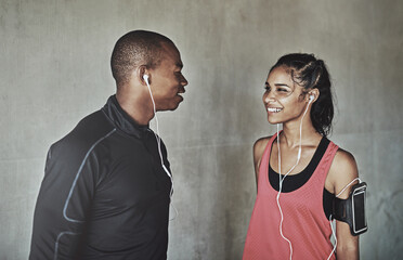Fitness, happy and couple with earphones by wall for running, exercise or training for marathon. Conversation, sports and athletes with audio tech for music with cardio workout for endurance in city.