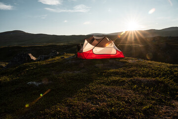 A wild campsite in Padjelanta National Park (Swedish Lapland) in amazing backlight during midsummer night. Red tent standing on the hill above Vaisaluokta.