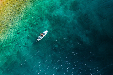 Top view of a woman moving through the sea with clear water, sitting on a paddle board. 