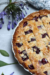 Delicious homemade pie with blueberries and almonds, summer flowers and leaves on light background, top view photo of fresh pastry item 