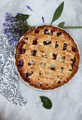 Delicious homemade pie with blueberries and almonds, summer flowers and leaves on light background, top view photo of fresh pastry item 