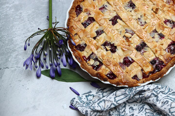 Delicious homemade pie with blueberries and almonds, summer flowers and leaves on light background, top view photo of fresh pastry item 