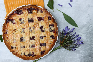 Delicious homemade pie with blueberries and almonds, summer flowers and leaves on light background, top view photo of fresh pastry item 