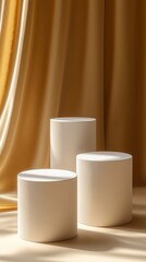 Three stylish cylindrical forms stand gracefully on a smooth surface, framed by flowing golden fabric, enhancing the serene atmosphere