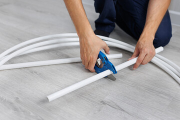 Plumber cuts a piece from a plastic pipe using a pipe cutter with a ratchet mechanism in close-up.