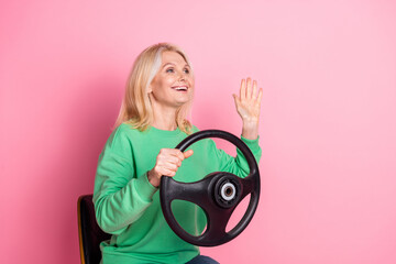 Photo portrait of lovely senior lady drive car wave hand dressed stylish green garment isolated on pink color background