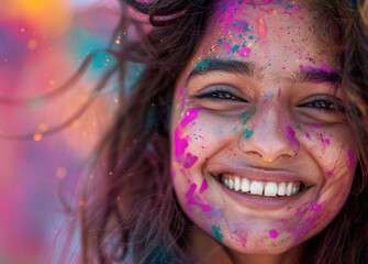 A beautiful Indian girl smiles while celebrating Holi, with colorful powder on her face and in her hair, against a background of vibrant festival colors