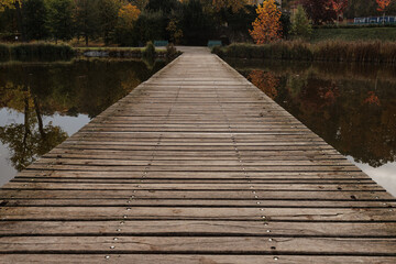 Fototapeta premium A wooden pier leads into calm waters in autumn Stromovka park, Prague, Czech republic