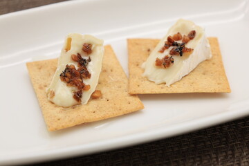 白い皿に盛ったクラッカーの上に切ったカマンベールチーズを乗せ、トッピングを加えたモノ