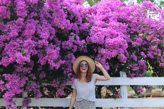 mulher com chap&eacute;u e &oacute;culos de sol em frente a flores roxas