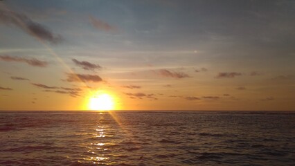A tranquil ocean sunset with the sun setting over the horizon, casting golden reflections on the water. The sky is painted with warm hues of orange and yellow, creating a peaceful atmosphere