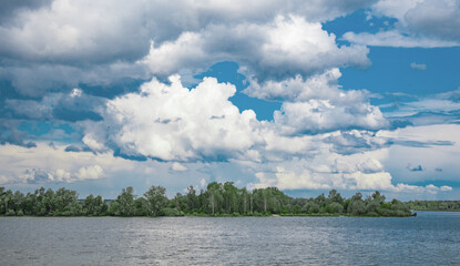 A forest on the riverbank under a blue cloudy sky, a calm summer landscape