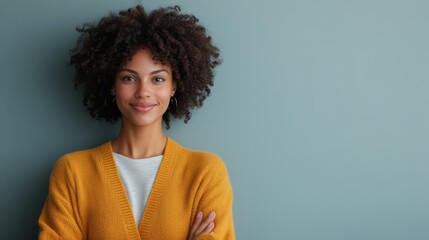 A self-assured woman with curly hair and a yellow cardigan stands against a green backdrop, exuding confidence, warmth, and a professional yet approachable demeanor.