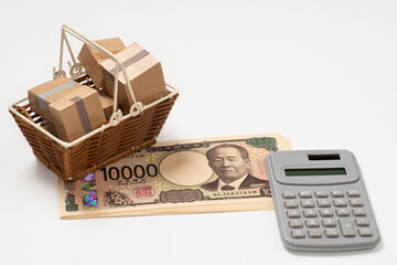 段ボール箱が入った買い物かごと日本円の一万円札の紙幣と電卓