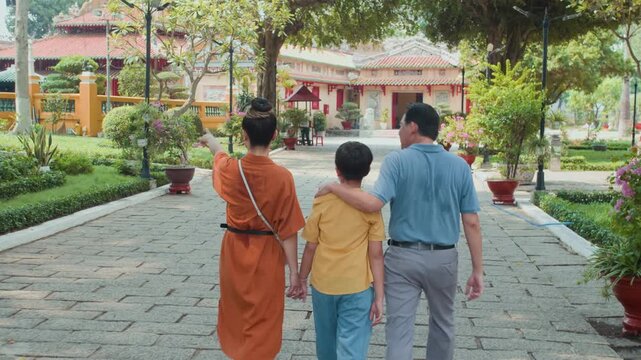 Back tracking shot of teenage son and his parents visiting Asian ancient temple